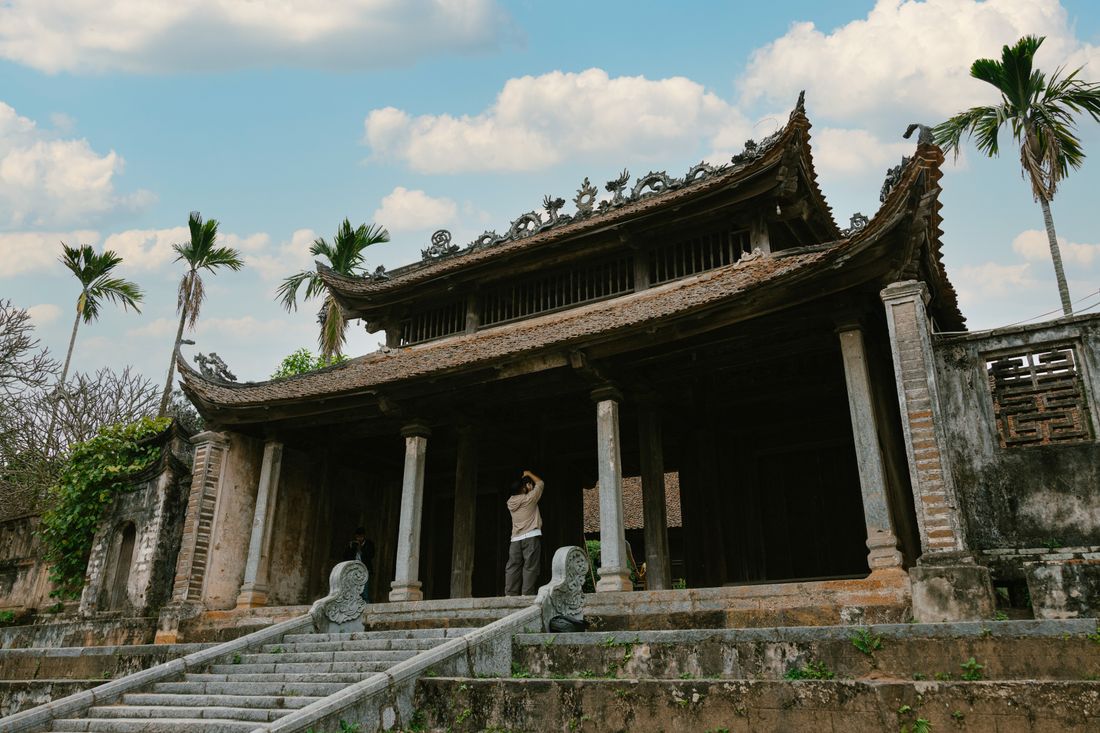 Đình làng Bắc Bộ nhìn từ sân: mái ngói rêu phong, đầu đao chạm rồng, hàng cột đá và bậc thềm