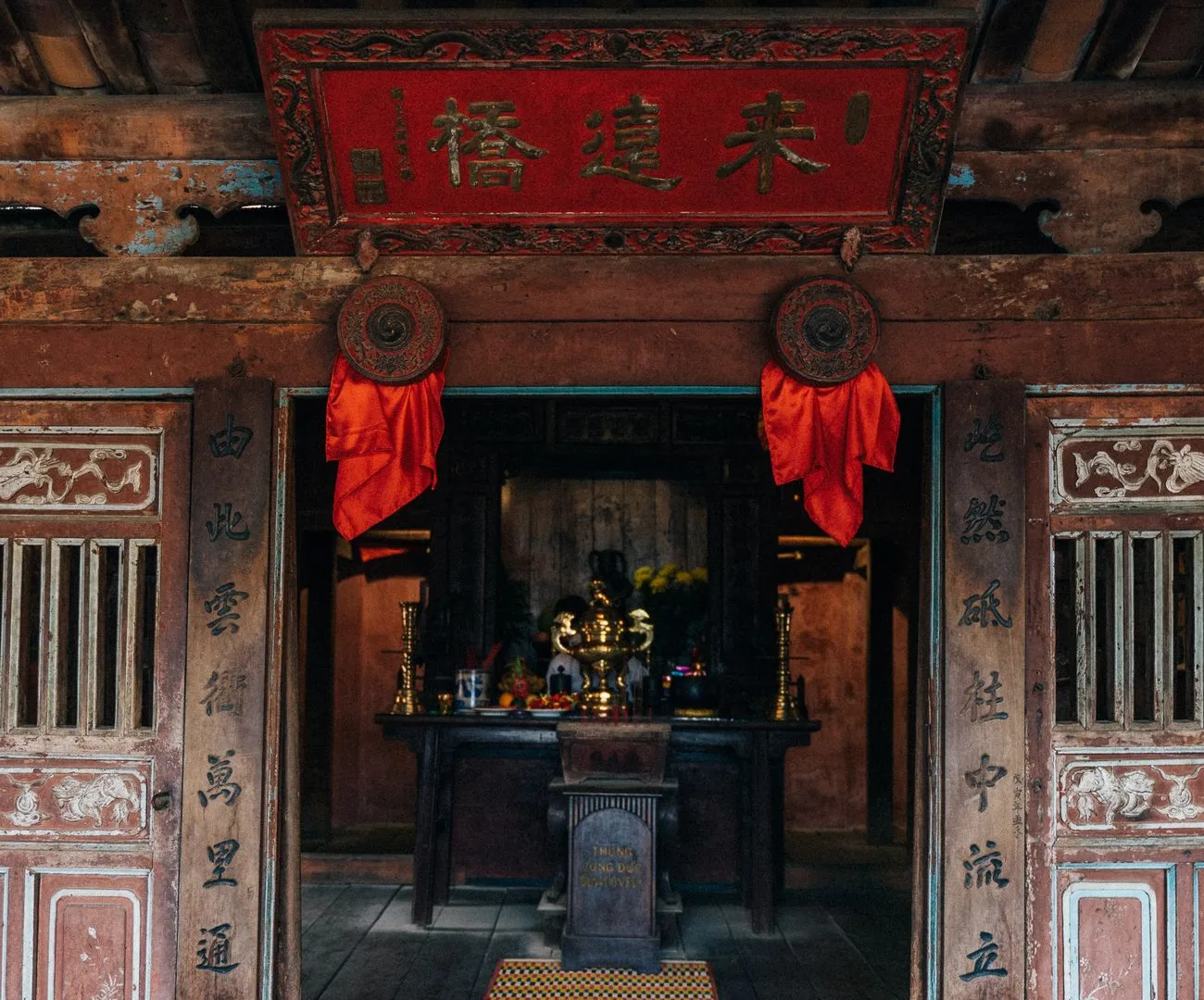 Gian giữa nhìn từ sân: hoành phi sơn son thếp vàng, câu đối trên hai cột, cửa bức bàn chạm và ban thờ tổ